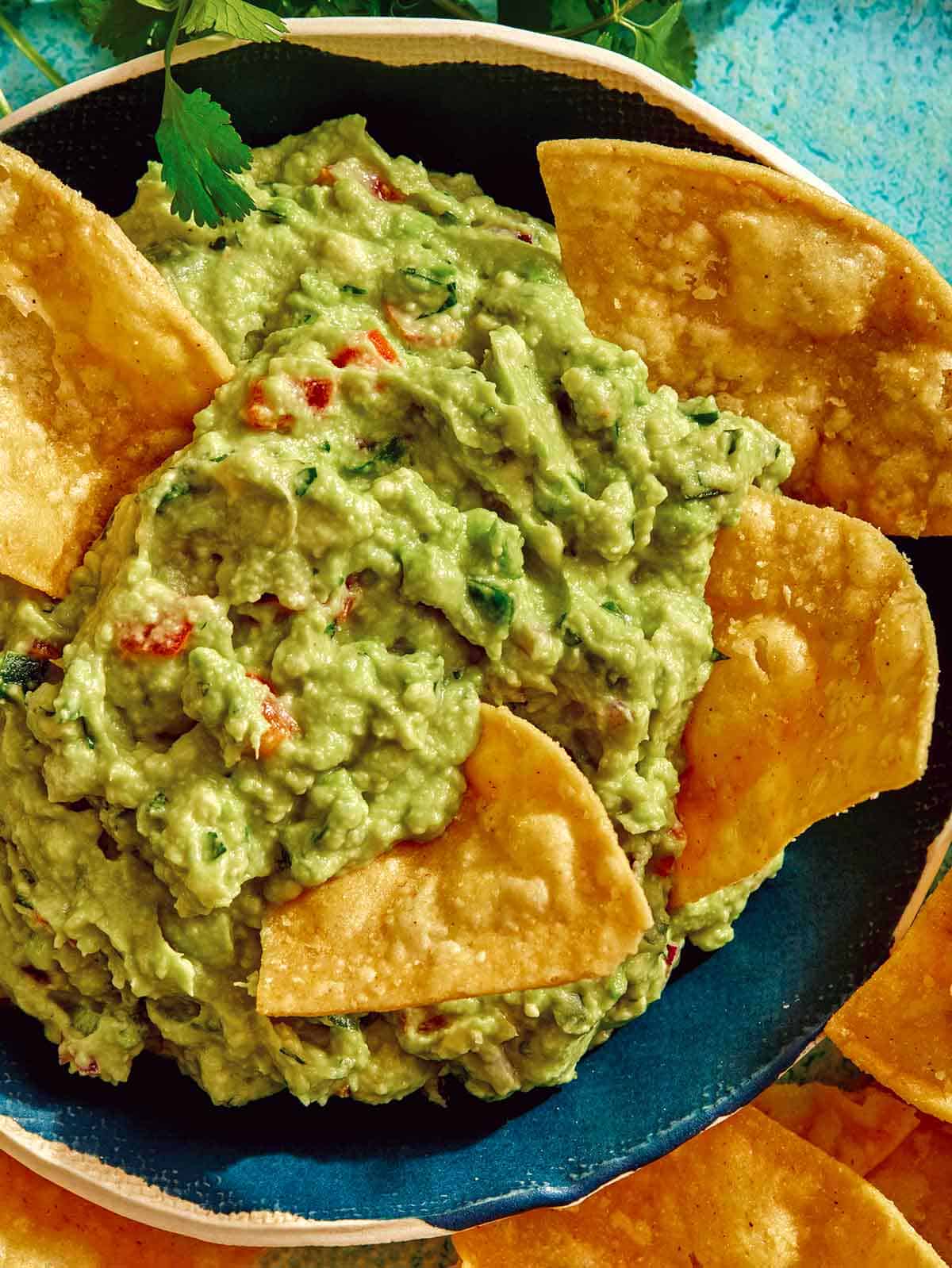 Up close photo of guacamole in a bowl with chips in the guacamole. 