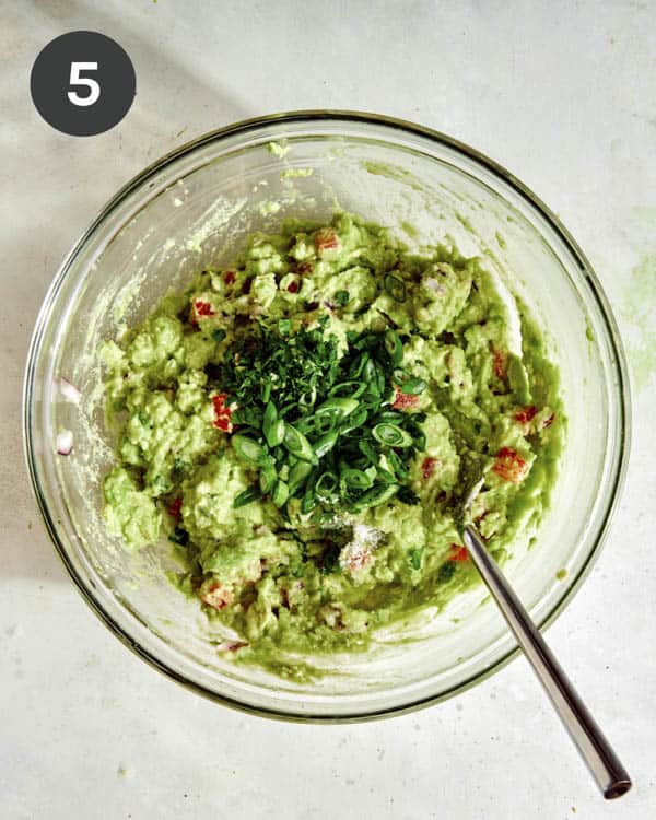 Guacamole in a glass bowl with onions being mixed in. 