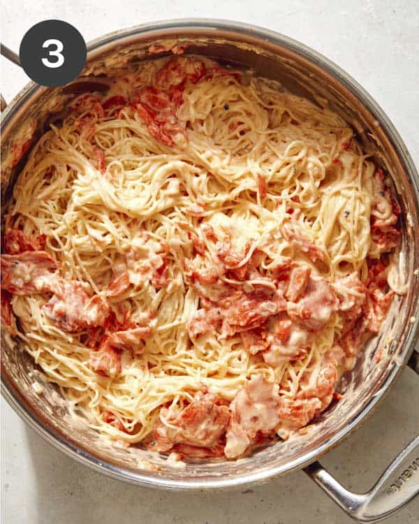 Smoked salmon pasta being tossed with a creamy sauce in a skillet. 