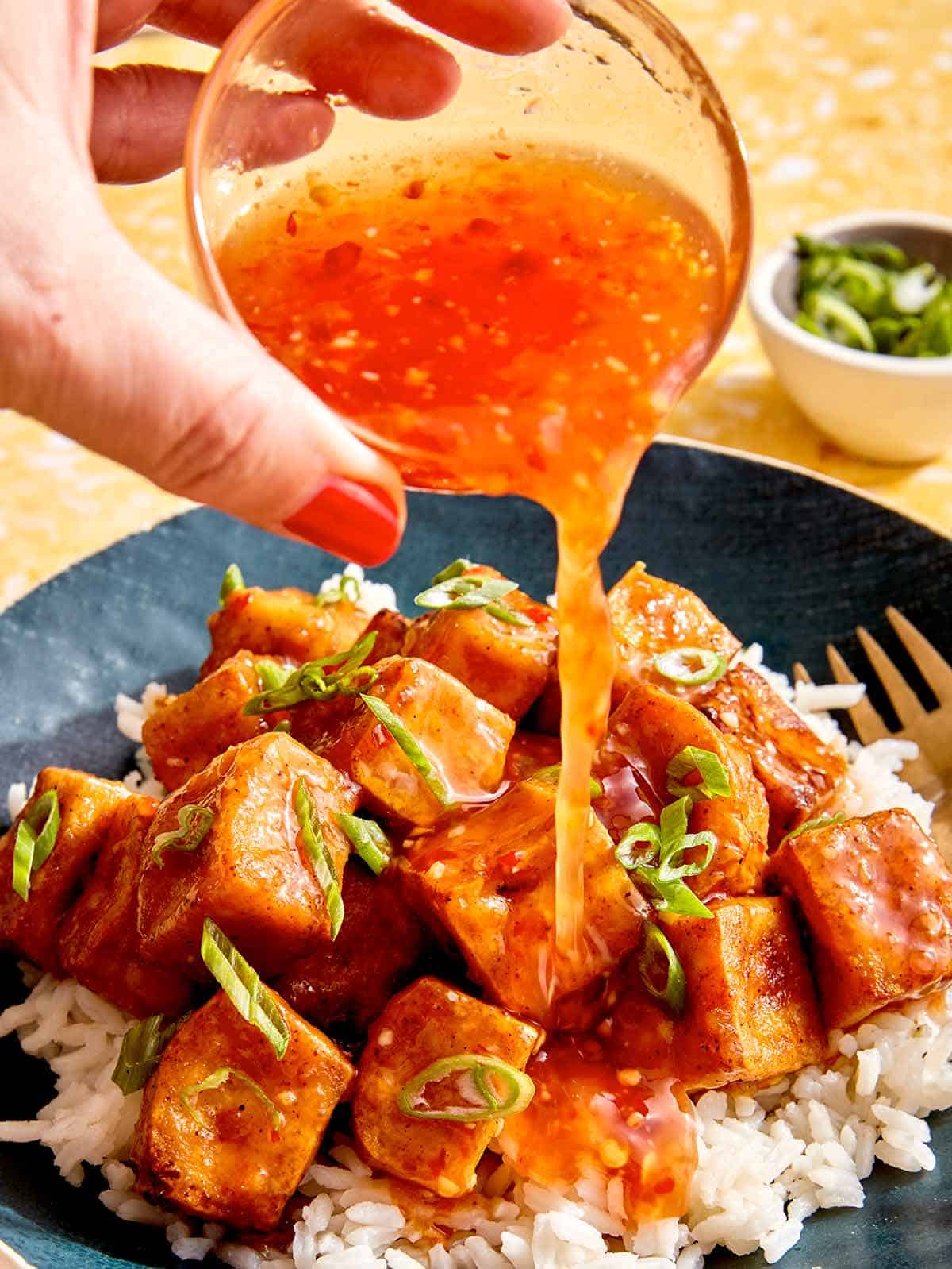 Sweet chili sauce being poured onto crispy tofu. 