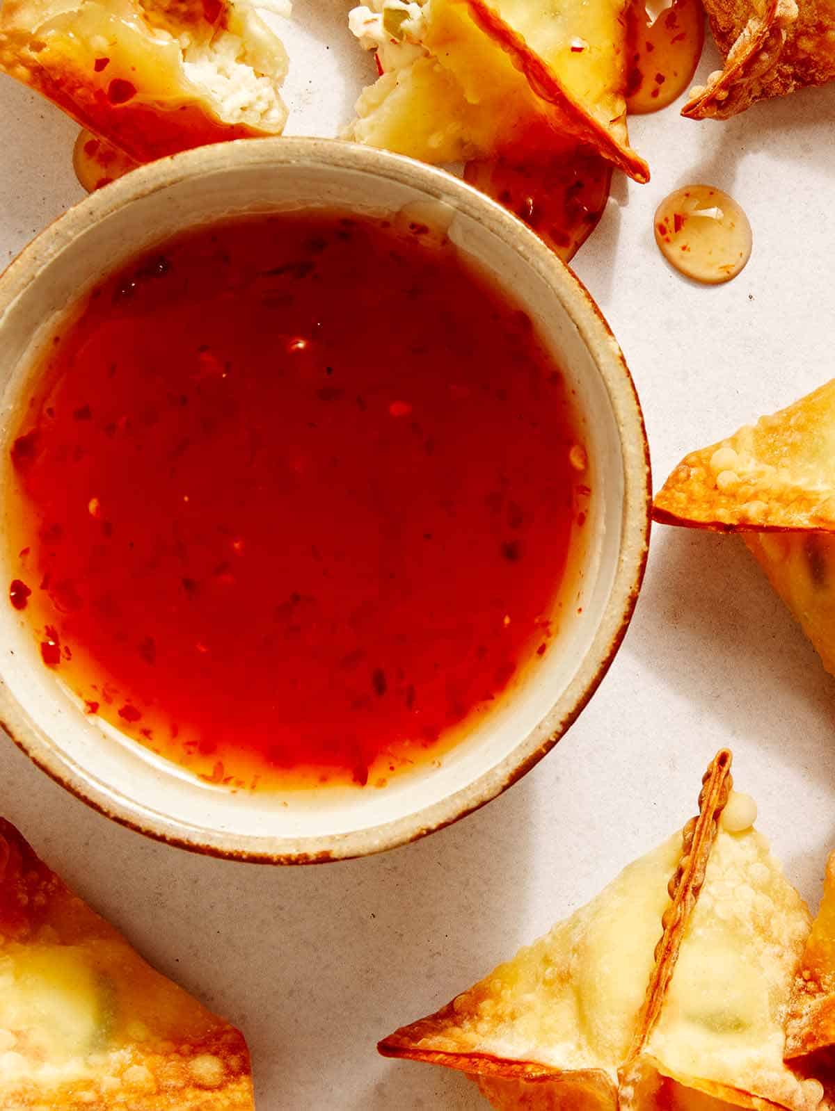 Sweet chili sauce next to some air fryer crab rangoon. 