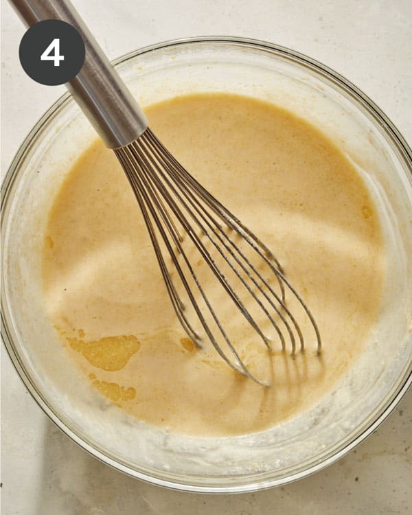 Spoon bread ingredients in a glass bowl with a whisk. 