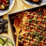 Salmon sushi bake in a baking dish with cucumbers and nori.