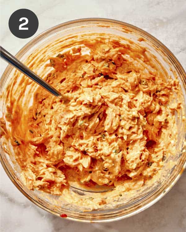 Cooked salmon mixed with mayo and sriracha in a glass bowl.