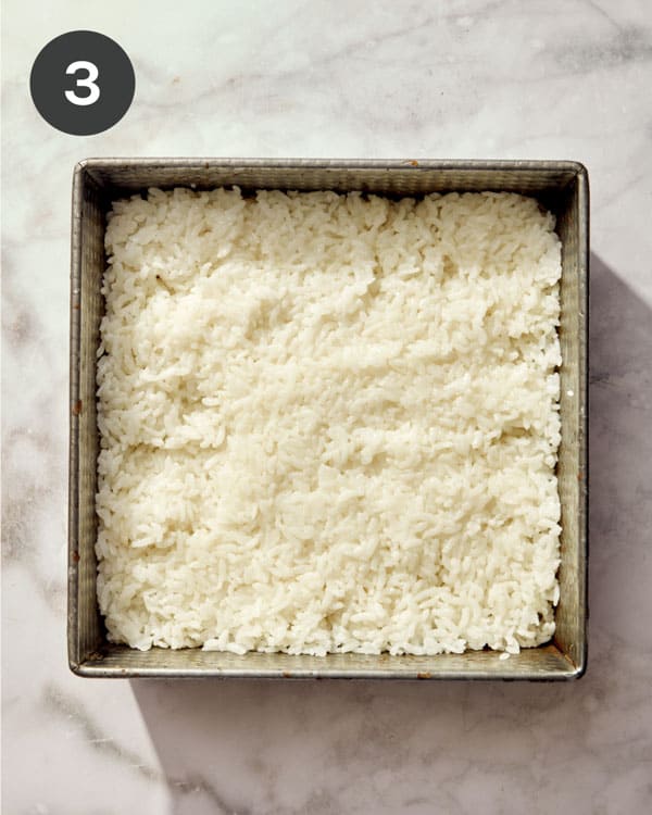 Rice being pressed into a baking dish to make a sushi bake.