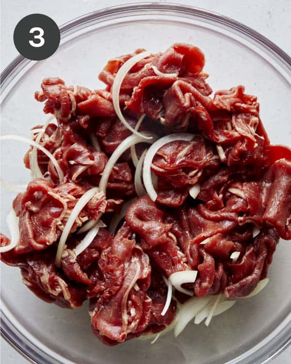Thinly sliced beef ribeye in a bowl with onion.