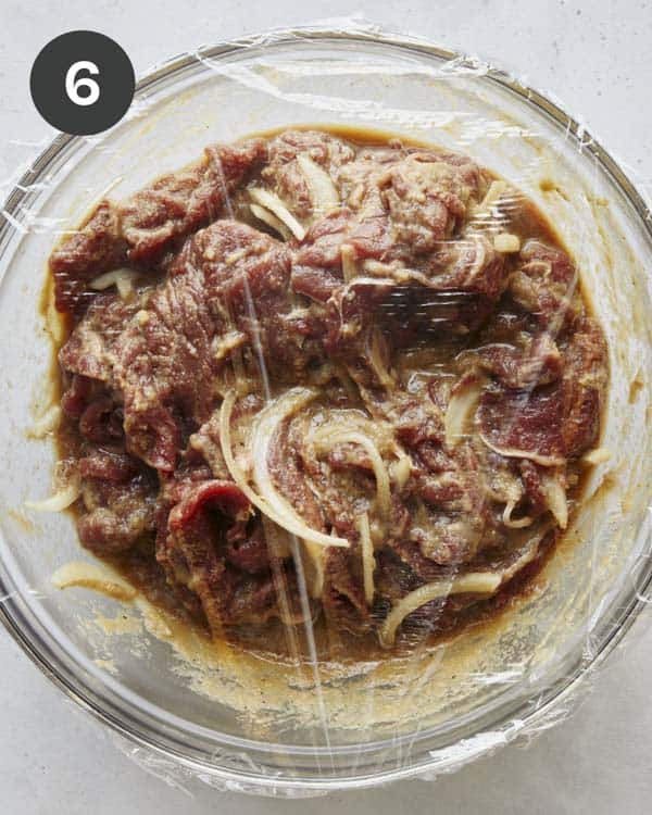 Beef marinating in a bowl with plastic wrap for Korean Beef Bulgogi.