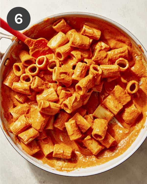 Rigatoni pasta being mixed with romesco sauce in a skillet. 