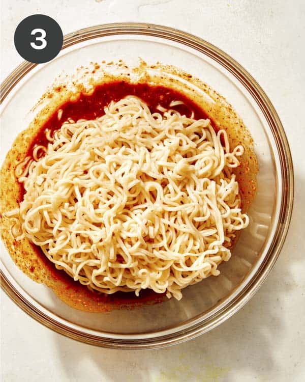 Ramen noodles in a glass bowl with spicy toss about to be tossed. 