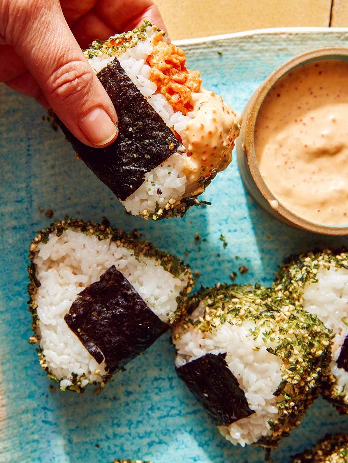 A hand holding a piece of onigri dipped in sauce.