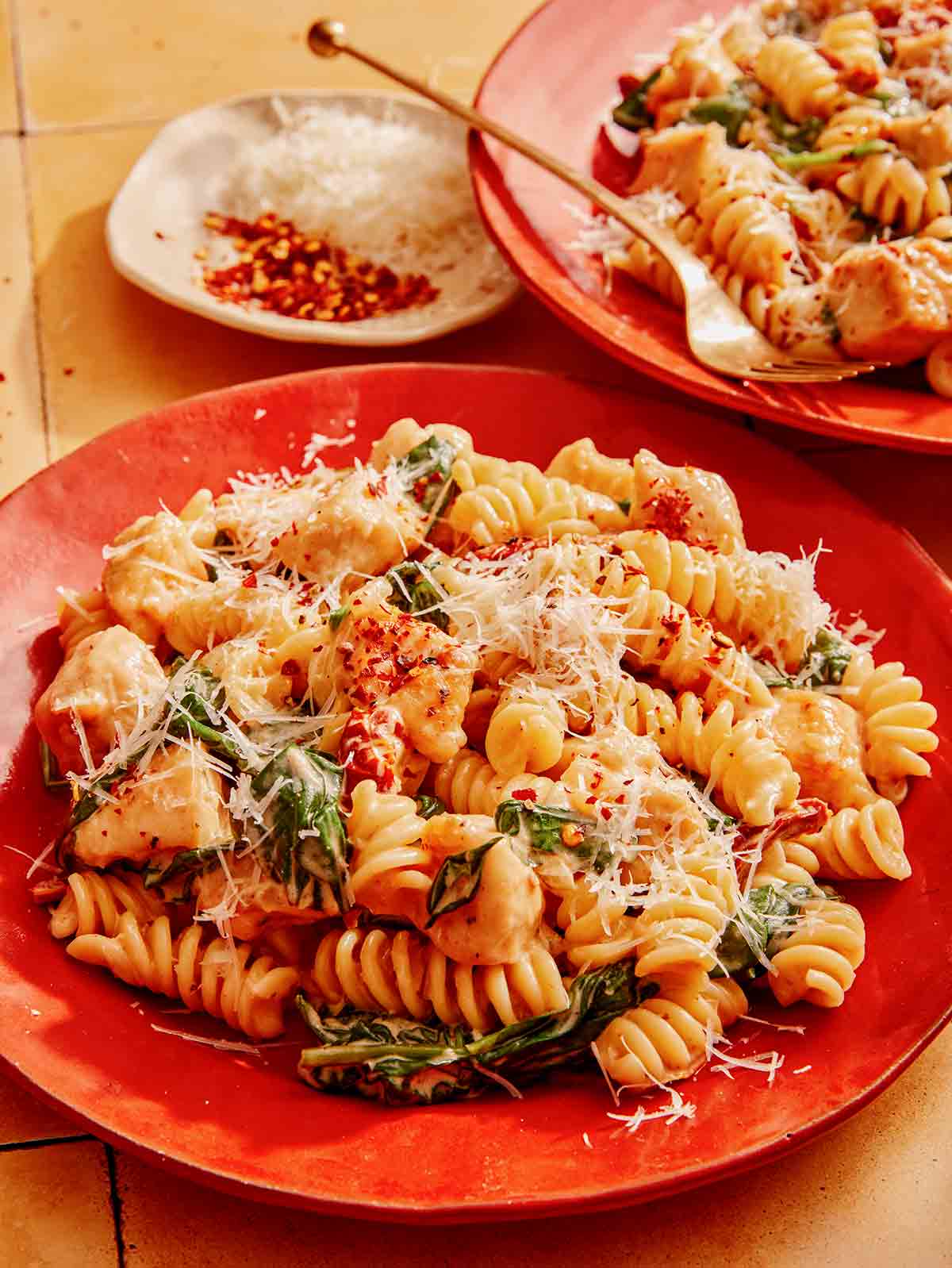 Tuscan chicken pasta on a plate with some red pepper flakes on the side. 