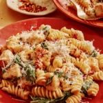 Tuscan chicken pasta on a plate with some red pepper flakes on the side.