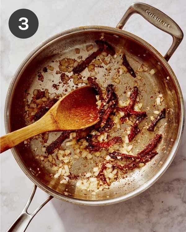 Garlic, onion, and sun dried tomatoes cooking in a skillet. 