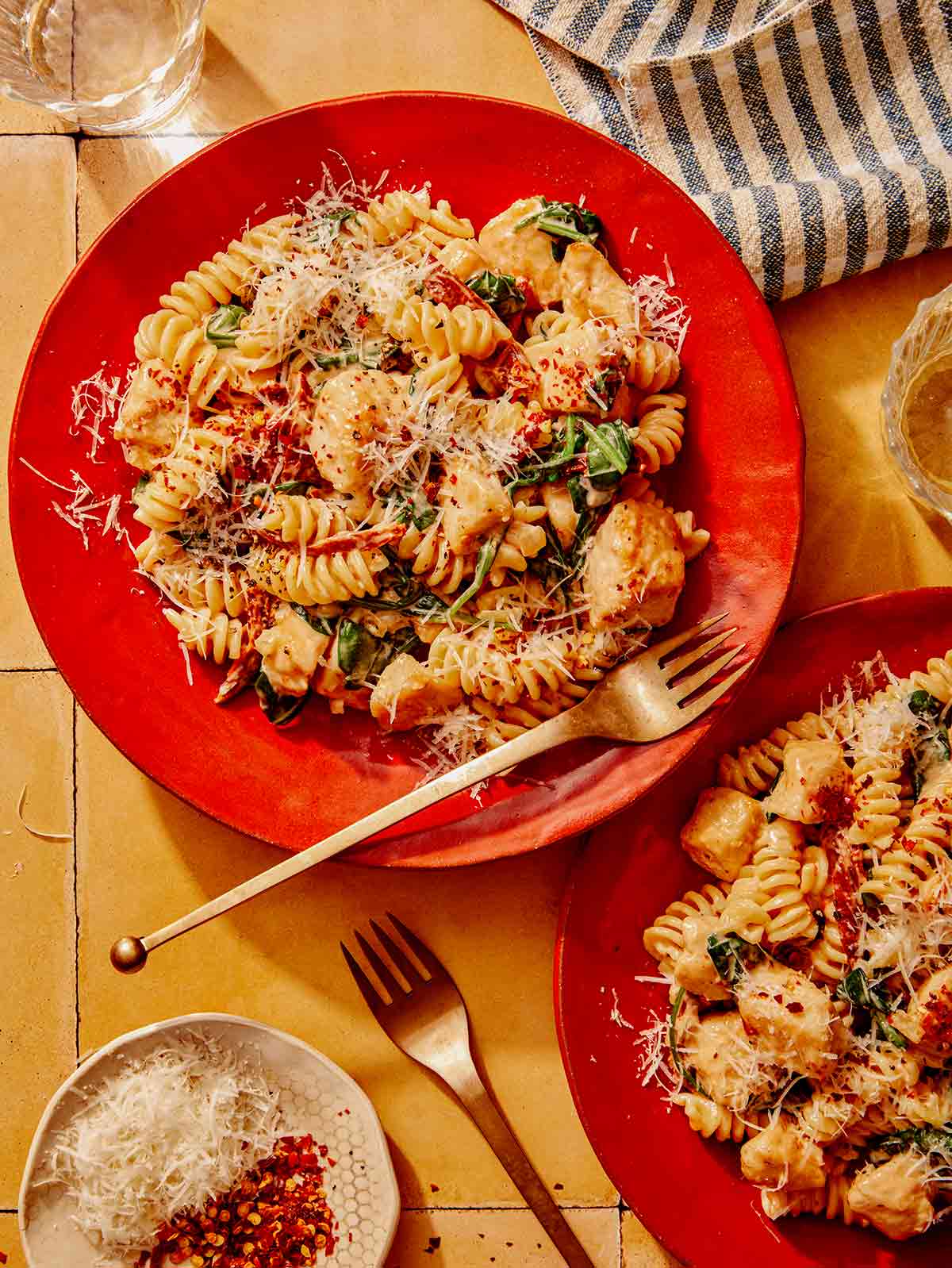 Tuscan chicken pasta on two plates with drinks and forks on the side. 