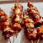 Air fryer bang bang chicken skewers on a platter with sauce being poured on top.