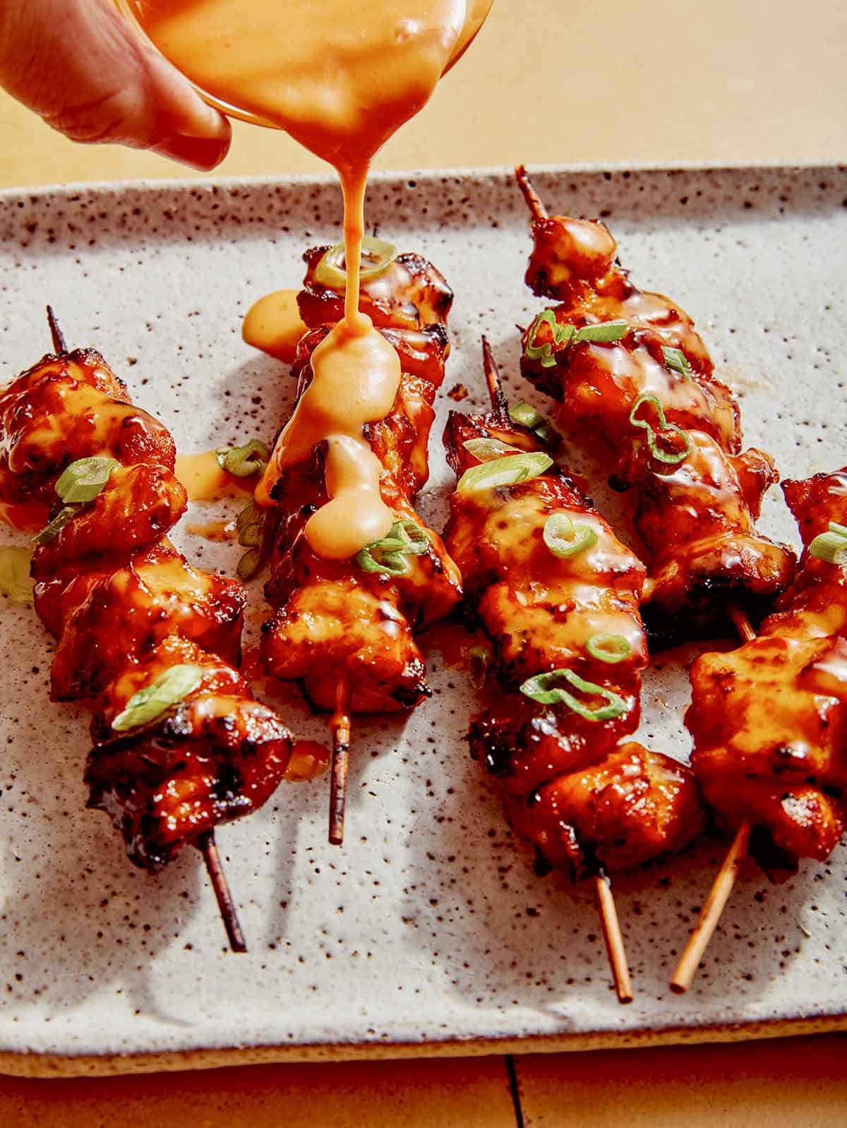 Oro gruzdintuvė bang bang vištienos iešmeliai ant lėkštės, ant kurio pilamas padažas. 