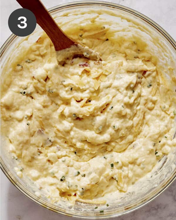 Corn casserole batter mixed together in a glass bowl with some mix ins.