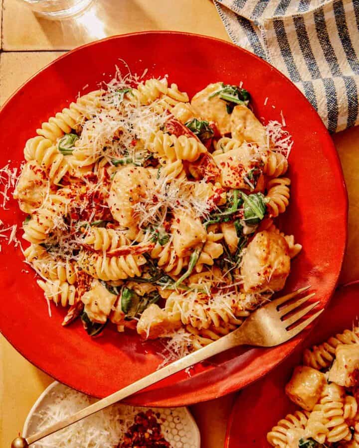 Tuscan chicken pasta on a plate with a fork next to it.