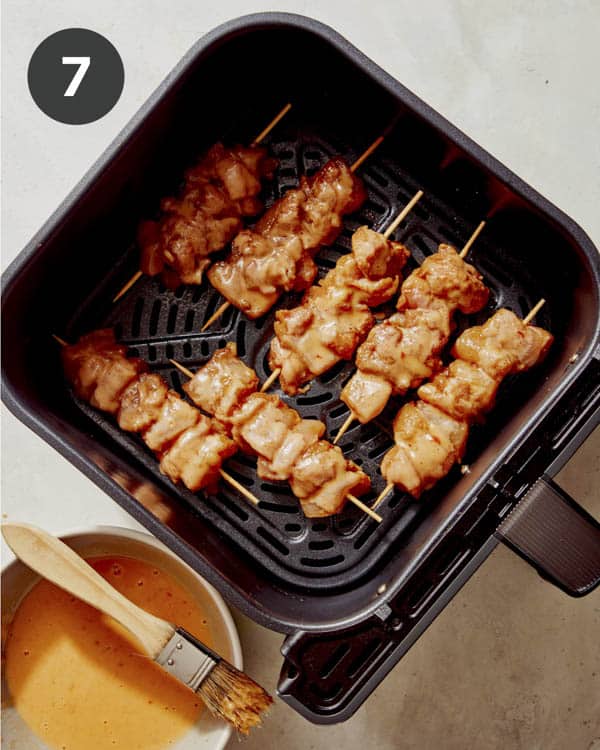 Basting chicken skewers in an air fryer basket.