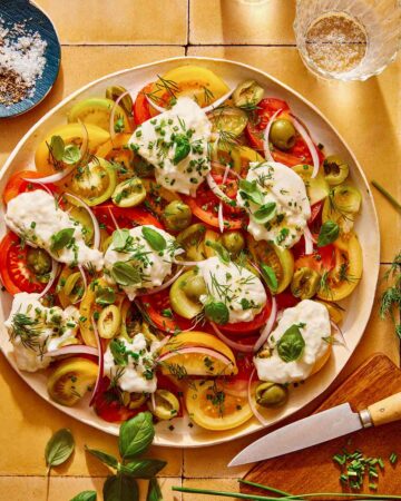 Tomato salad on a plate with herbs on the side.