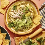 A bowl of soup with a cutting board of garnishes next to it.