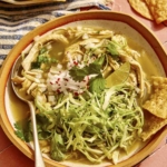 Chicken pozole verde in a bowl with garnishes and chips on the side.