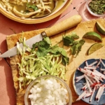 Chicken pozole verde in a bowl with garnishes and chips on the side.