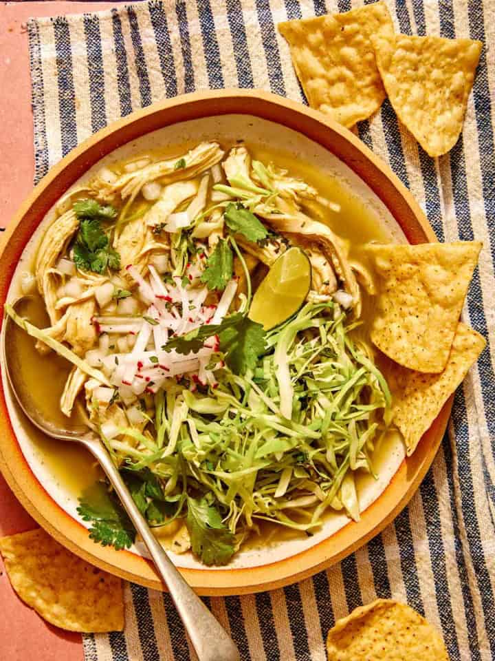 Chicken pozole verde in a bowl with chips on the side.