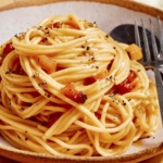 Carbonara in a bowl with a spoon and fork next to it.