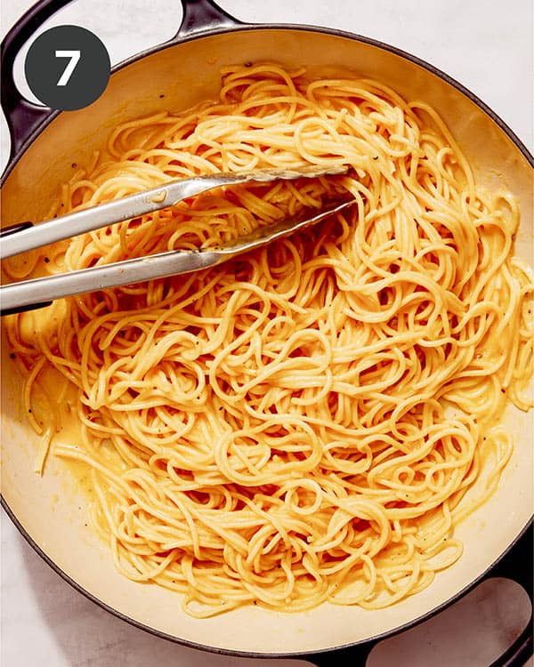 Pasta being tossed with a carbonara mixture in a skillet.
