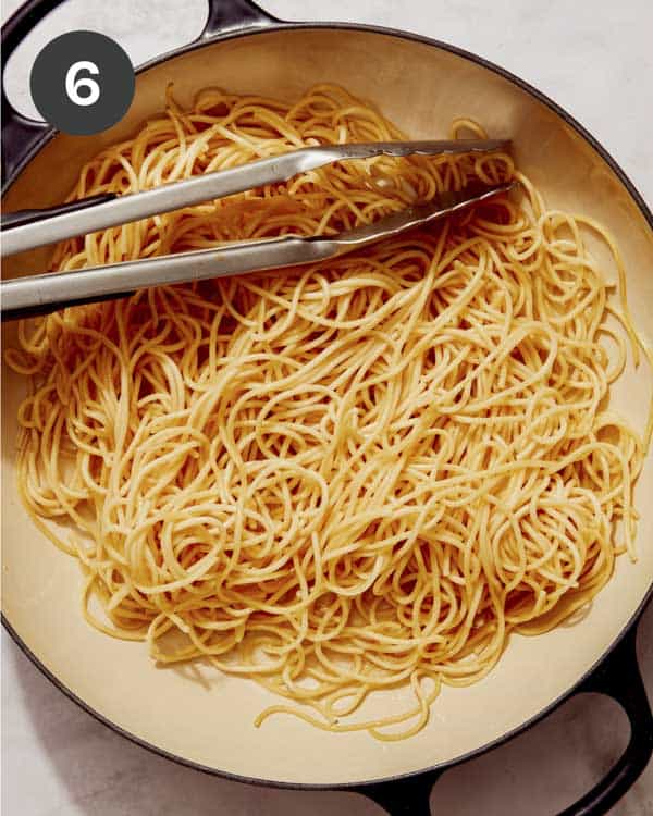 Pasta being tossed in pork fat in a skillet.