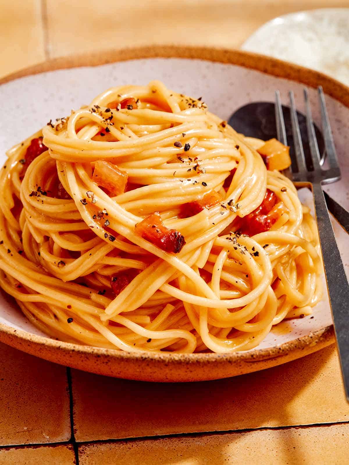 Carbonara dubenyje su šaukštu ir šakute šalia.