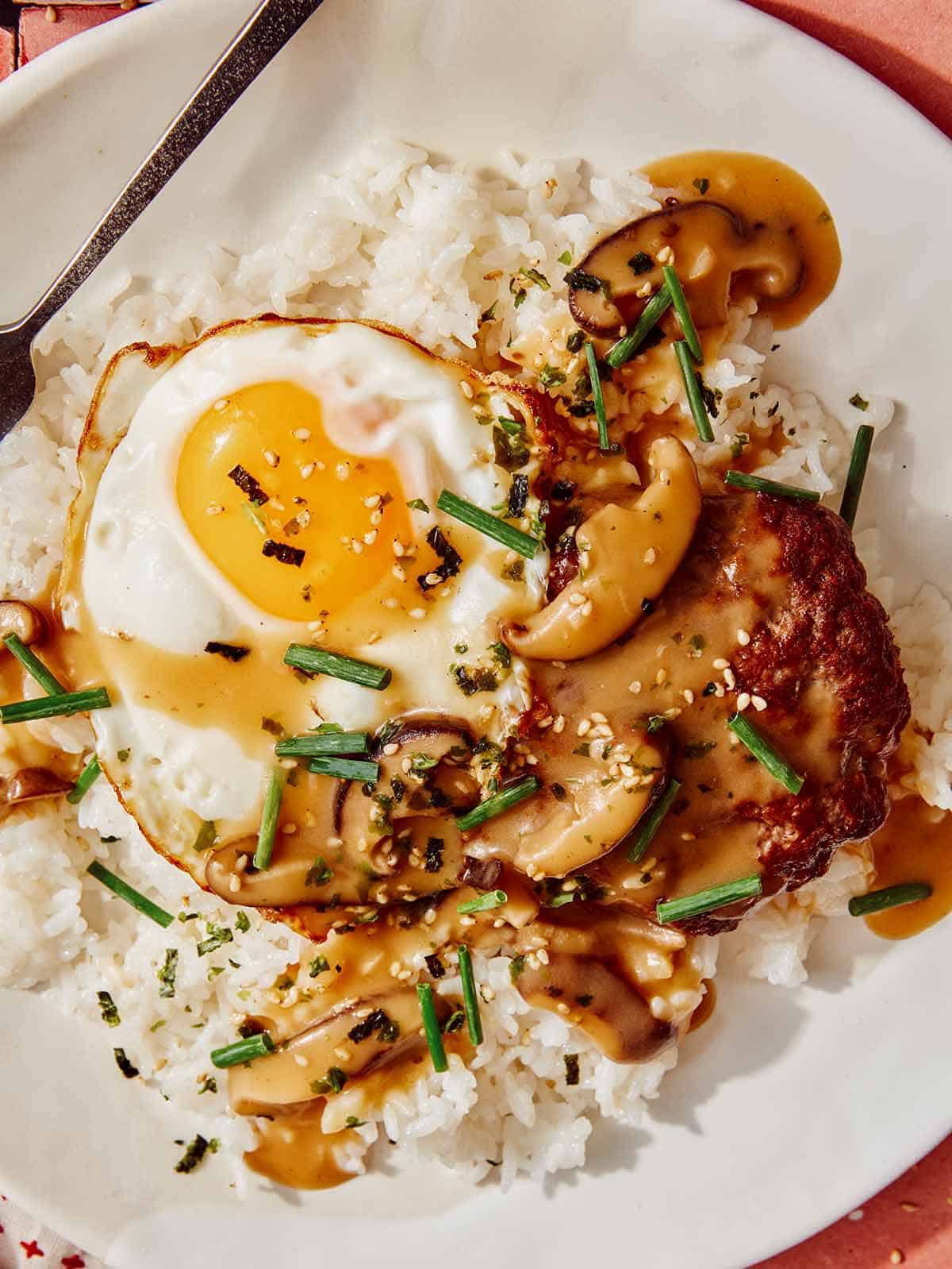 Loco moco iš arti ant lėkštės su šakute šalia.