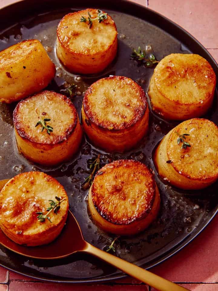 Fondant potatoes on a platter with a spoon.