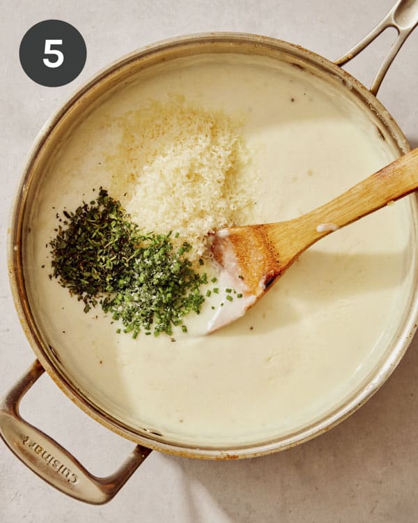 A creamy sauce with parmesan and fresh herbs being added to it.