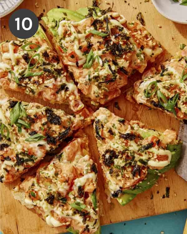 Sushi pizza cut into slices on a cutting board.