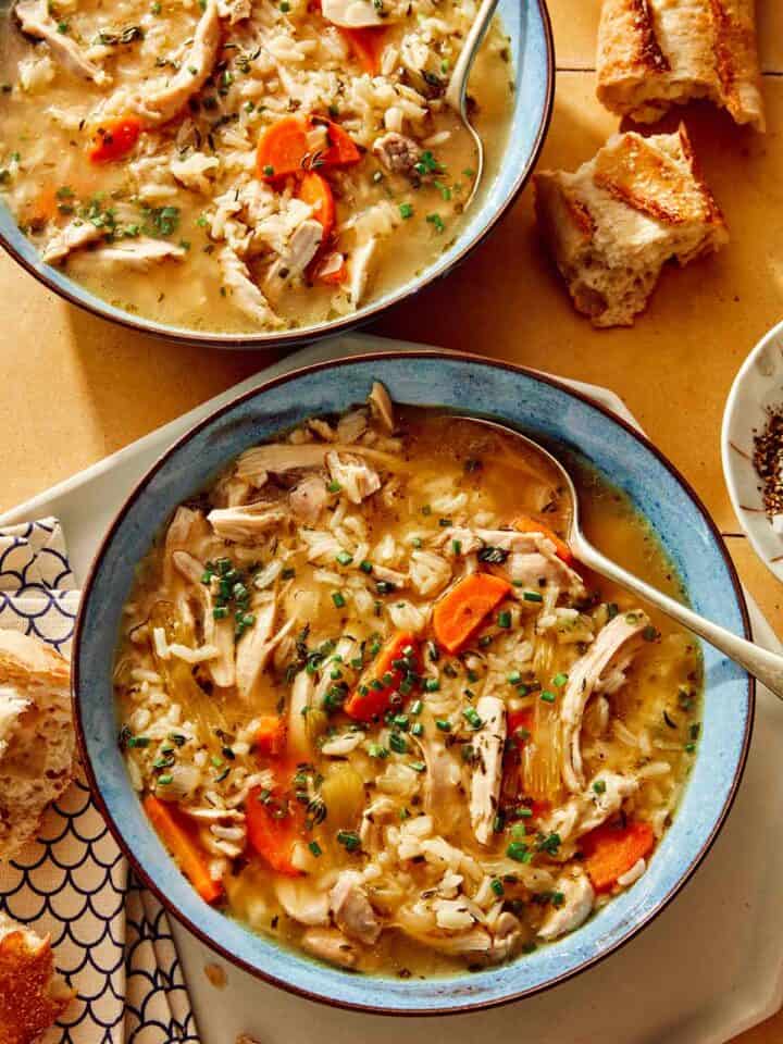 Chicken and rice soup in two bowls with bread on the side.