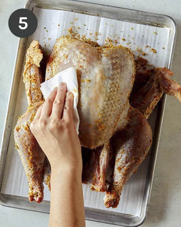 Wiping off a dry rub from a raw turkey on a baking sheet.