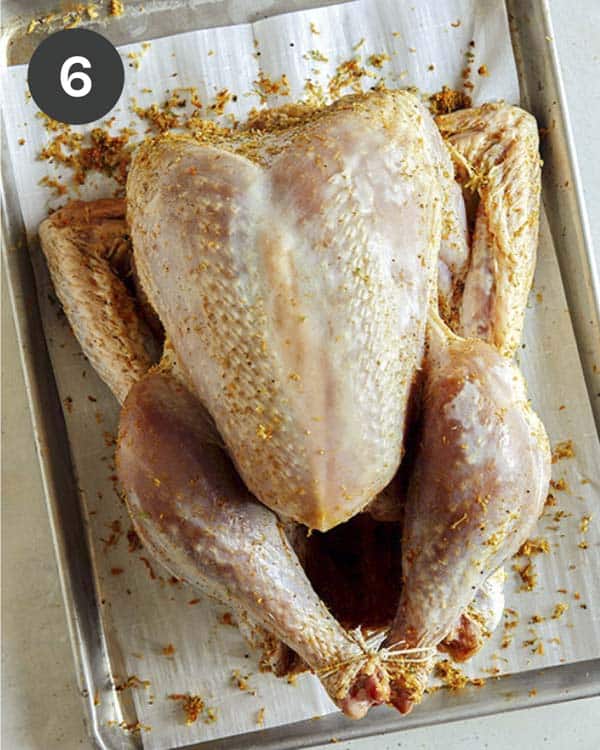 A raw turkey on a baking sheet with citrus dry brine.