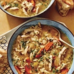 Chicken and rice soup in two bowls with bread on the side.