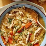 Chicken and rice soup in two bowls with bread on the side.