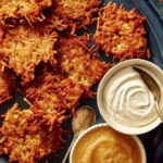 Potato latkes on a platter with plates to serve next to it.