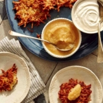 Potato latkes served from a platter with toppings of sour cream and applesauce.