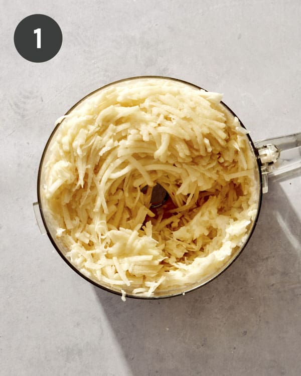 Shredded potatoes in the bowl of a food processor.