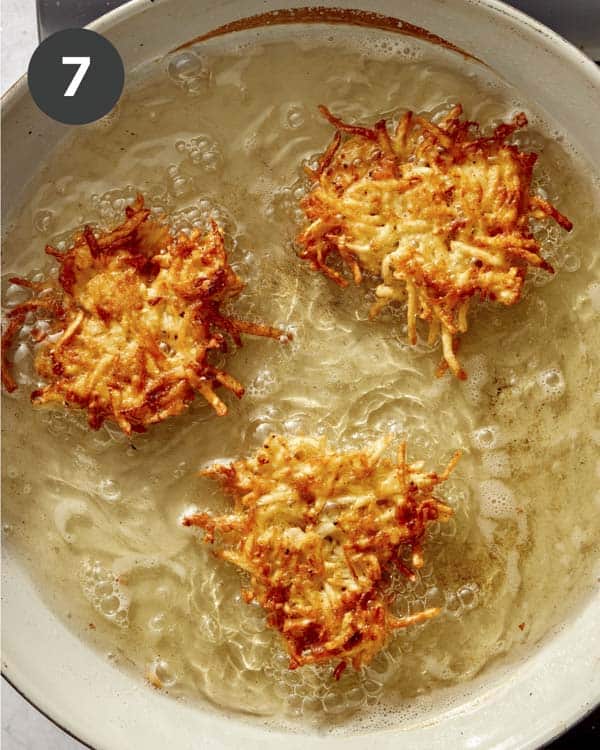 Potato latkes cooking in hot oil after they have been flipped.