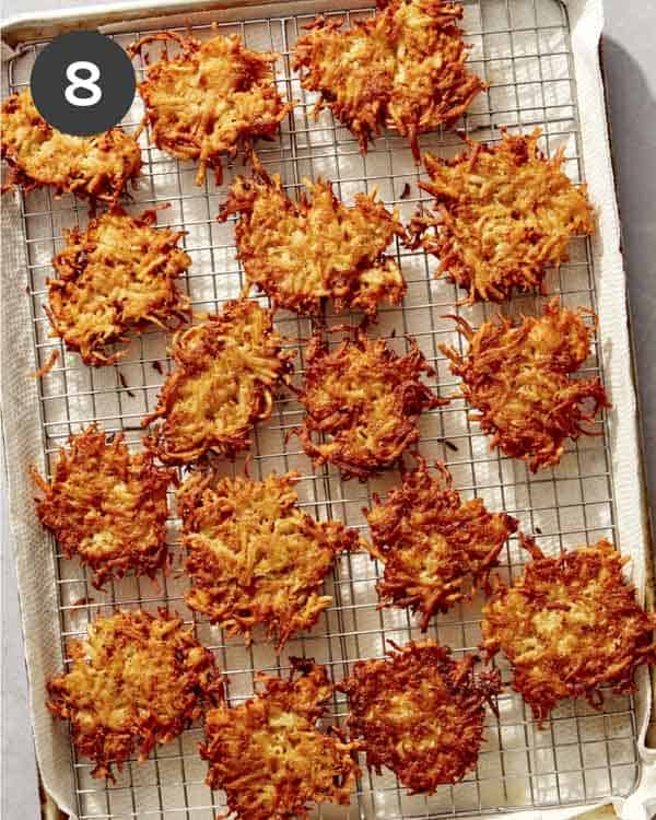 Potato latkes on a cooling rack with a paper towel underneath.
