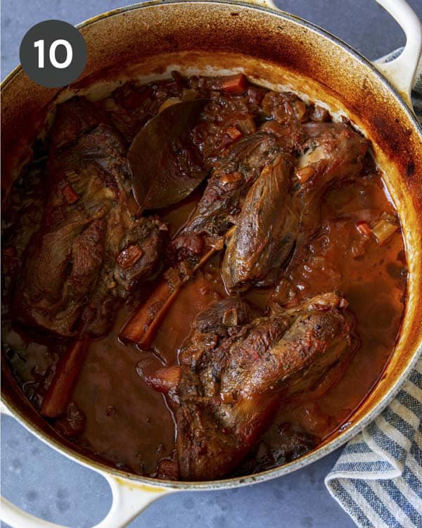 Braised lamb shanks in a large pot.