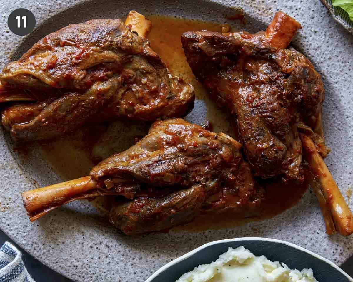 Braised lamb shanks on a platter with mashed potatoes on the side.