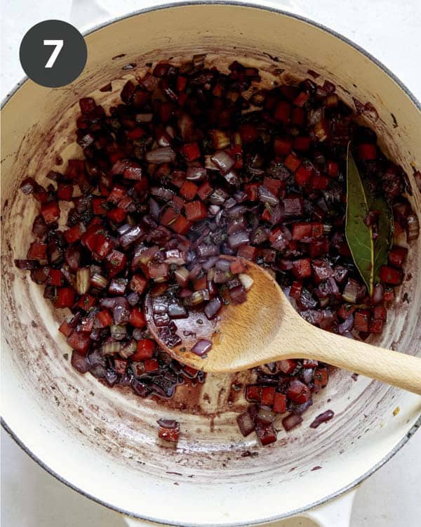 Red wine deglazing a pot of vegetables.
