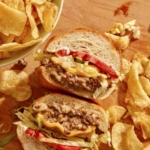 A chopped cheese sandwich cut in half on a cutting board.